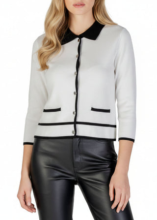 Woman wearing a white cardigan with black trim and black leather pants on a white background