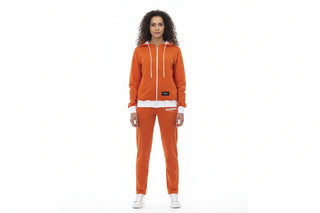 A woman modeling a matching orange zip-up hoodie and jogger pants set with white accents, including drawstrings, hem trim, and white sneakers, against a plain white background.